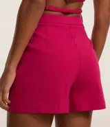 Short pollera corto en bengalina color fucsia, con superposición asimétrica en el delantero y pequeño bolsillo. Cierre lateral con cremallera.