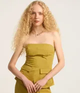 Blusa sin breteles color amarillo mostaza, confeccionada en sarga, con cierre por cremallera invisible en el lateral y bolsillos con solapa en la parte del frente. Posee lastex en la espalda y bajo redondeado.