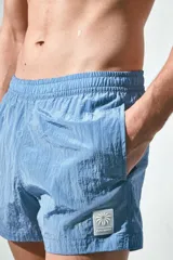 Short de baño azul de nylon con elástico revestido y cordón para ajustar oculto en la cintura, bolsillos laterales y bolsillo de solapa con cierre autoadherente atrás. Largo por encima de la rodilla con abertura corta en los laterales y suspensor interior en malla suave.
