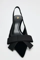 Zapato destalonado de terciopelo negro con tacón fino y adorno de lazo en la parte delantera.