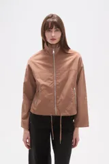 Campera de corte holgado en color tostado, confeccionada en poliamida. Presenta cuello alto, cierre frontal con cremallera, bolsillos laterales con cierre y cordón ajustable en el ruedo.