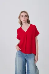 Blusa de poliéster color rojo vibrante, con escote en V profundo y pinzas frontales que generan un efecto drapeado. Presenta mangas cortas y un calce holgado.