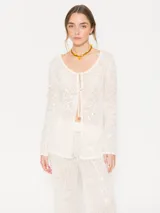 Cárdigan de tejido calado color crema con lentejuelas, de silueta liviana y femenina. Presenta escote redondo y cierre frontal con lazos finos.