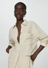 Camisa color crema de bambula con cuello camisero, diseño oversize, manga larga con puños abotonados, bolsillo de parche en la parte delantera y cierre delantero con botones.