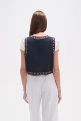 Chaleco sin mangas, sin abroches, con escote redondo. Confeccionado en tejido oscuro con bordados geométricos y florales en tonos rojos, blancos, azules y mostaza, con apliques de cuentas.