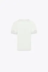 Camiseta blanca de algodón con textura de canalé, escote en pico y mangas cortas. Detalle de encaje blanco en escote y mangas.