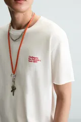 Camiseta blanca de corte recto, cuello redondo y manga corta. Estampado pequeño en el frente y estampado grande en la espalda con texto en color rojo.
