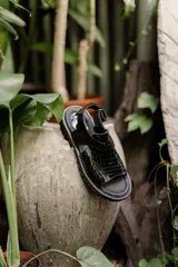 Sandalia de cuero sintético negro con diseño de tiras anchas cruzadas en el empeine y tira con hebilla al tobillo.