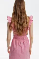 Vestido corto rosado en tejido de algodón con broderie, escote recto, breteles anchos fruncidos, cuerpo entallado con frunces elásticos y pollera con leve vuelo. Ribete de volados en escote y breteles. Forrado.