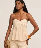 Blusa color beige sin breteles, confeccionada en viscolino con 15% de lino, con escote corazón, fruncidos y lastex en la espalda. La prenda tiene cuerditas aplicadas en el busto.