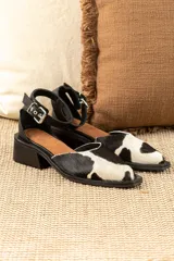 Sandalias bajas de cuero con estampado animal print de vaca en blanco y negro, con pulsera al tobillo y taco cuadrado.