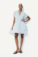 Vestido túnica corto blanco con estampado floral azul, cuello mao y abertura en V. Mangas cortas con doblez, botones forrados y costura fruncida en la cadera. Corte holgado.