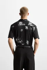 Camisa negra con estampado floral en tonos grises, de manga corta y cuello bowling.