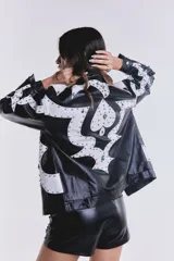 Campera de cuero sintético negra con apliques blancos y tachas plateadas.