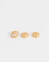 Set de tres anillos dorados de metal con diferentes diseños: uno con tres aros abiertos, otro con tres aros lisos y otro con dos aros lisos.