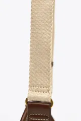 Bolso mini color crudo con detalles en marrón. Tiene asa de mano y doble asa bandolera extraíble, una en tejido tipo canvas y otra con pespunte. Incluye charm con piezas metálicas y bolsillo interior con cremallera.