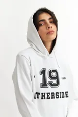 Hoodie gris con capucha y cordones ajustables. Estampado frontal con la palabra 'OTHERSIDE' y las siglas 'OTH' en azul marino.