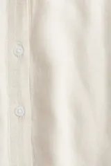 Camisa color crema en tejido liviano de lino y viscosa con cuello, botones adelante y pliegue de caja invertido en la espalda. Modelo de corte holgado con hombros marcadamente caídos, mangas al codo y bajo levemente redondeado.