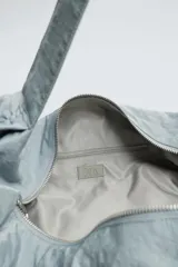 Bolso de hombro acolchado celeste de tejido técnico con cierre de cremallera. Tiene un bolsillo interior con cremallera y asa ajustable.
