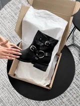 Botas cortas de cuero negro con arnés desmontable y hebillas plateadas.