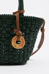 Bolso tipo tote de mimbre color marrón oscuro, con doble asa corta y correa de cuero marrón. Incluye dije circular dorado con letras grabadas.