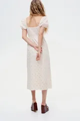 Vestido largo de algodón color crudo con estampado de pequeñas flores rosas, escote cuadrado, mangas cortas abullonadas con elástico y cuerpo fruncido.
