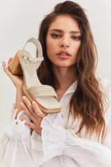 Sandalias de tacón color beige con puntera cuadrada, tiras doradas en el empeine y tobillo, y taco cuadrado.