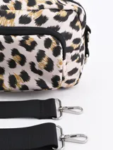 Bandolera rectangular con estampado animal print de leopardo en tonos beige, negro y dorado. Tiene un bolsillo frontal con cierre y correa larga regulable.