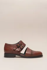Zapato de cuero color marrón, estilo sandalia cerrada con puntera brogue y dos tiras ajustables con hebillas negras. Tiene un taco bajo y grueso de color negro.