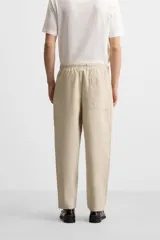Pantalón de hombre color beige, corte carrot fit, con cintura elástica ajustable con cordón, bolsillos frontales y bolsillo trasero de plastrón.