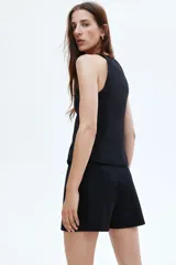 Short pollera negro de tiro alto con diseño cruzado tipo pareo y cinturón fijo con hebilla revestida. Presenta cierre oculto y cierre de corchete en un lateral.