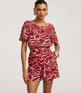 Enterito corto de poliéster con estampado abstracto en tonos borgoña y blanco. Tiene mangas cortas, escote redondo, cierre en la espalda, elástico en la cintura y lazo para ajustar.