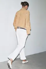 Pantalón cropped color beige de tiro alto y corte recto, confeccionado en algodón. Cuenta con bolsillos delanteros y traseros, trabillas en la cintura y cierre frontal con cremallera y botón.