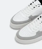 Championes urbanos de cuero sintético blanco con recortes en gris y negro, cierre con cordones y suela de goma.