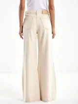 Pantalón acampanado color crema, de tiro alto, con cierre y botón. Tiene dos bolsillos delanteros y dos traseros.