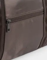 Bolso color beige de tela deportiva con manijas superiores y cierre superior. Tiene un bolsillo frontal con cierre y bolsillos laterales con cierre y tiradores de cordón y goma.