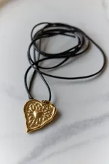Collar con tiento encerado negro y dije dorado con forma de corazón texturizado.