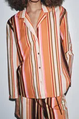 Camisa de manga larga con cuello solapa y cierre frontal con botones. Diseño a rayas verticales en tonos naranja, marrón, rosa y blanco.
