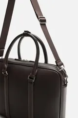 Maletín negro con textura grabada, cierre de cremallera, bolsillo interior para dispositivos electrónicos de hasta 13 pulgadas, bolsillo frontal con cremallera, doble asa de mano y asa de hombro ajustable y extraíble.