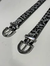 Cinturón con estampado animal print en blanco y negro, con hebilla metálica plateada.