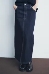 Falda larga de jean azul oscuro, de tiro alto y corte recto. Tiene cinco bolsillos, trabillas en la cintura, pespuntes a contraste, abertura en la parte trasera y cierre frontal con cremallera y botón metálico.