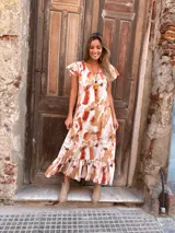 Vestido largo con estampado abstracto en tonos camel, naranja y blanco, con escote en V, mangas cortas con volados y falda con volados en el ruedo.