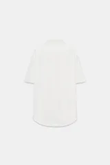 Camisa color beige de cuello solapa y manga corta. Tiene dos bolsillos delanteros con solapa y cierre frontal con botones.