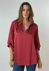 Blusa manga 3/4 color borgoña de seda con cuello tipo camisa y detalle de cierre dorado en el escote.