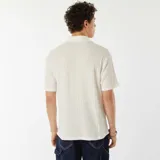 Camisa de manga corta color beige con textura de punto calado, cuello clásico y cierre frontal con botones.