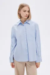 Camisa a rayas verticales verdes y blancas, de corte holgado, manga larga con puños abotonados, cuello clásico y bolsillo de parche en el pecho.