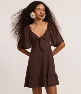 Vestido corto evasé color marrón chocolate, con escote corazón, nudo en el escote, mangas cortas con volados, lastex en la espalda y volado en el bajo.