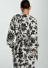 Blusa blanca con estampado floral negro, de tejido fluido, cuello de tira y cierre de lazo.