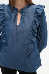 Blusa blanca de calce holgado con cuello en V y lazo frontal. Presenta detalles de volados en el pecho y cuello, y mangas largas con puños elásticos.