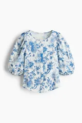 Blusa blanca con estampado floral azul, cuello redondo, cierre de botones y mangas globo tres cuartos con puños elásticos.